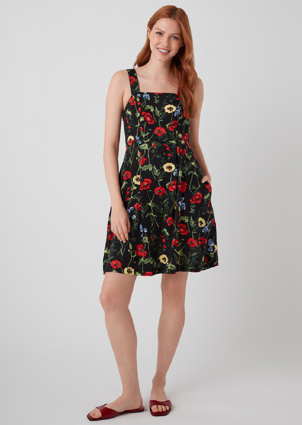 A woman in a floral dress stands against a plain background.