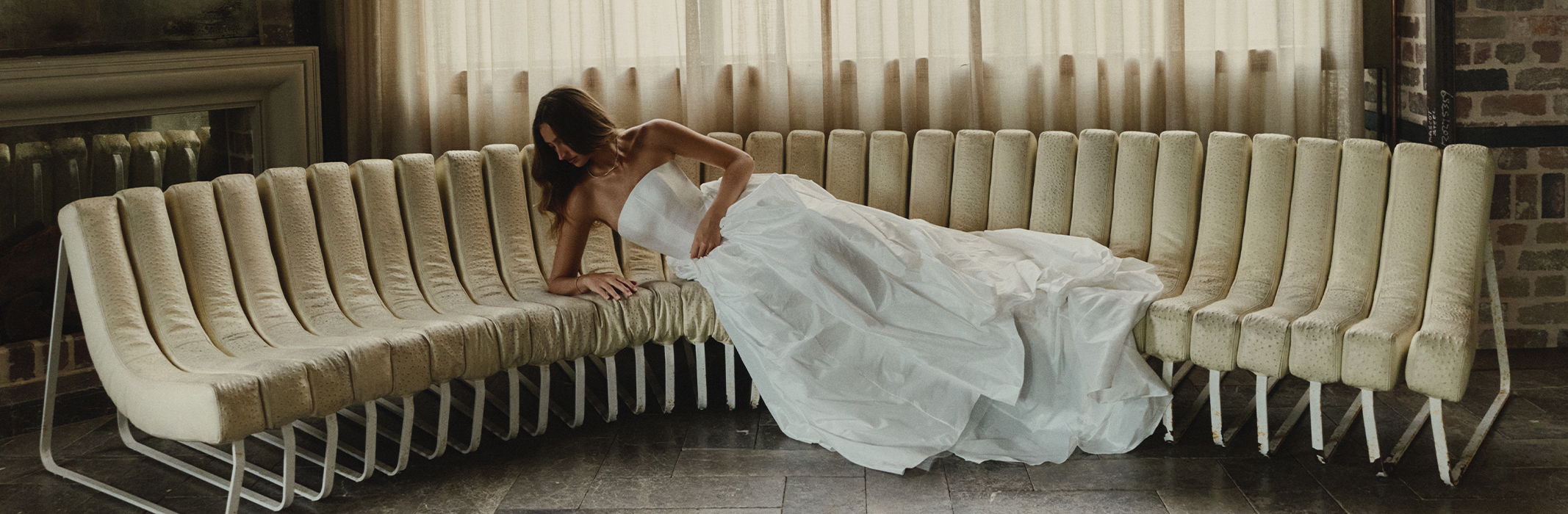 Woman in a wedding dress reclining on a curved row of white chairs.