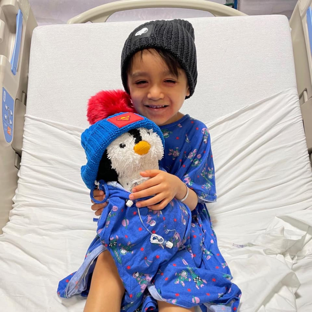 Small boy in a hospital bed holding a stuffed penguin wrapped in a blue blanket
