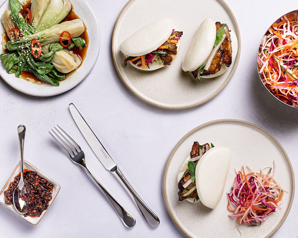 Plates of pork belly bao buns, vegetables, and colorful slaw.