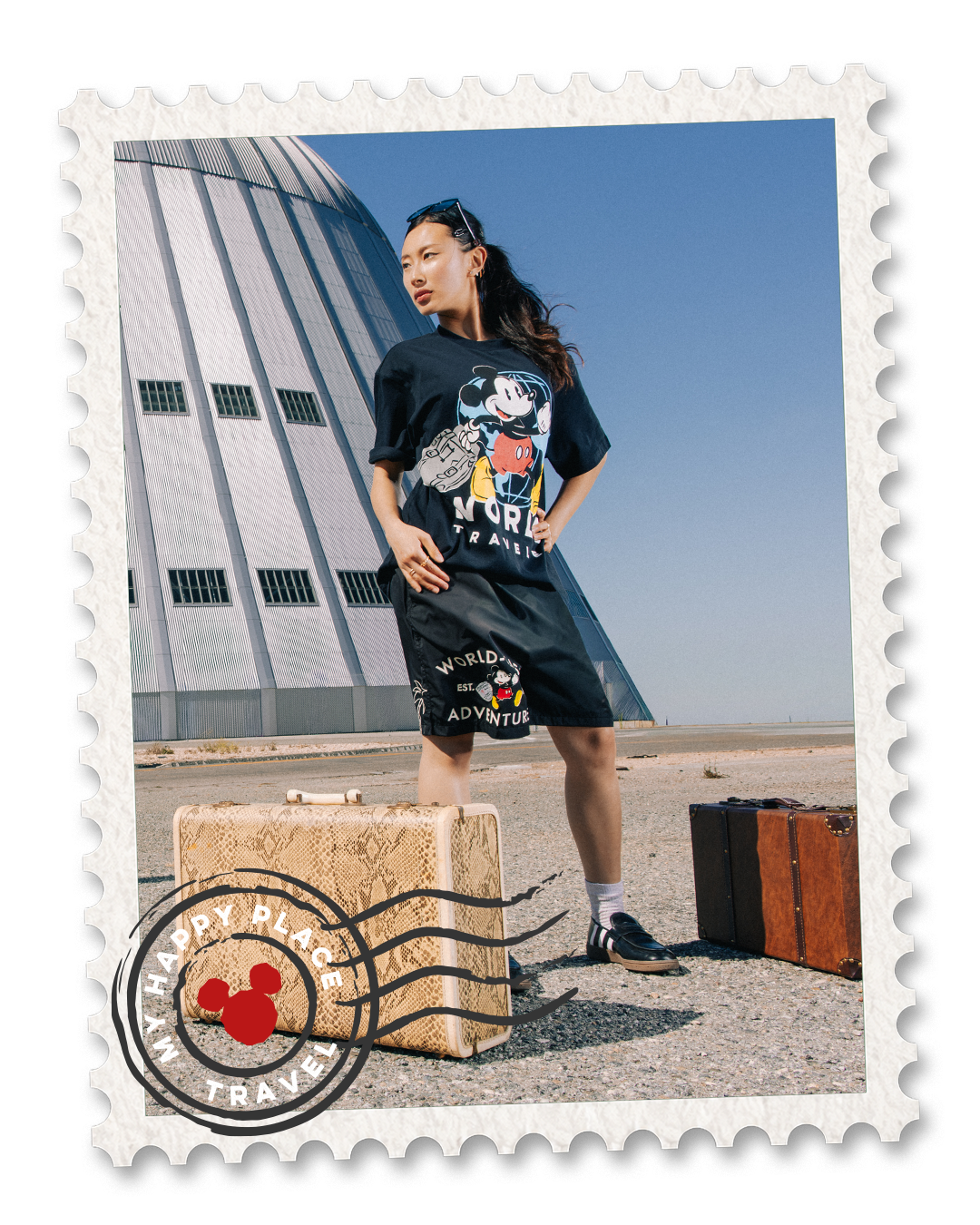 Person posing in a graphic t-shirt near suitcases and a large structure.