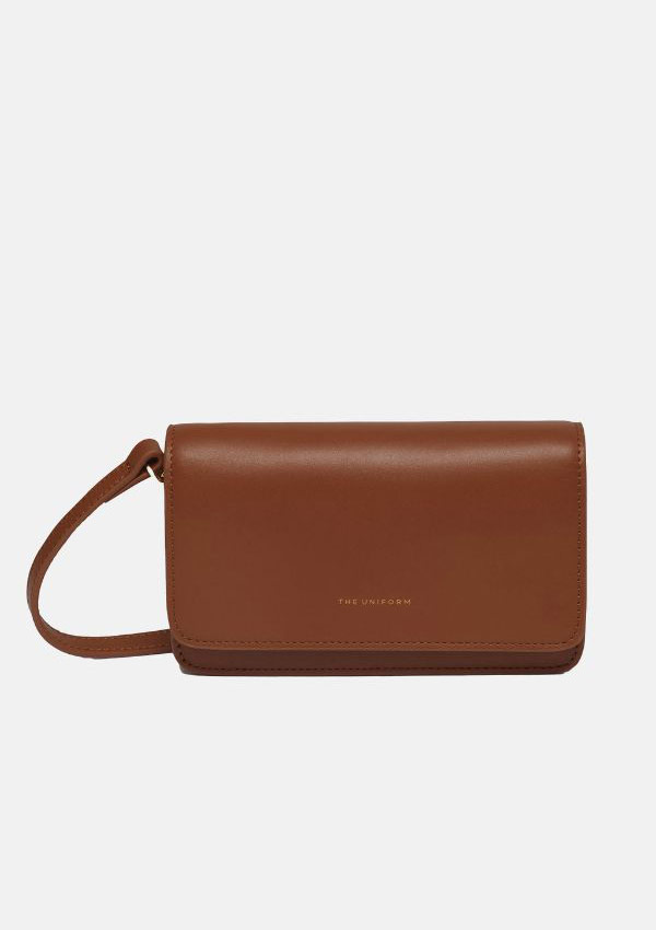 Product image of The Uniform Essential Bag in mid cocoa brown. A small, leather envelope bag with a thin shoulder strap and 'The Uniform' embossed in small gold letters on the front.