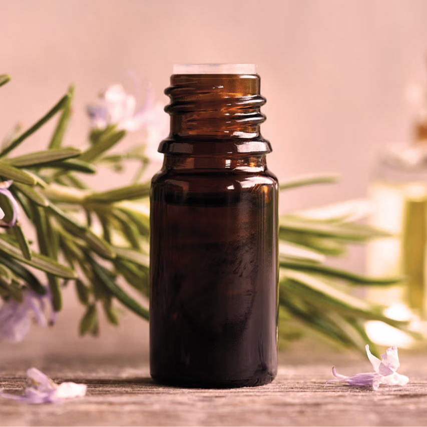Brown essential oil bottle with rosemary sprigs and flowers in the background.