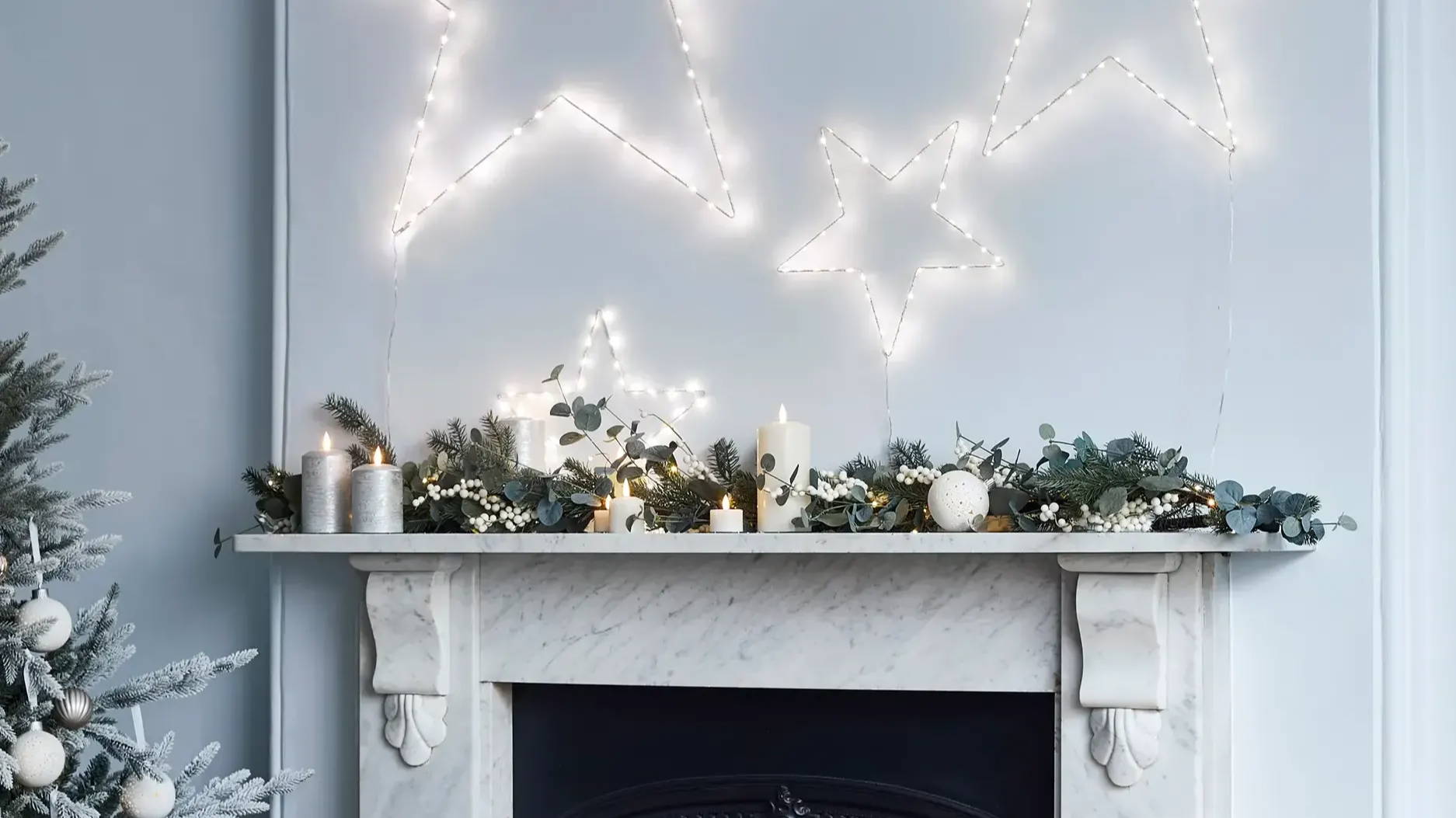 Mantle piece with a garland and candles and a trio of star lights above. 
