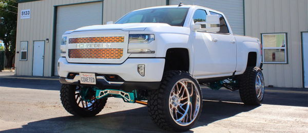 Front three-quarter Jacob's lifted white Chevrolet Silverado with teal suspension and chrome wheels photo 1