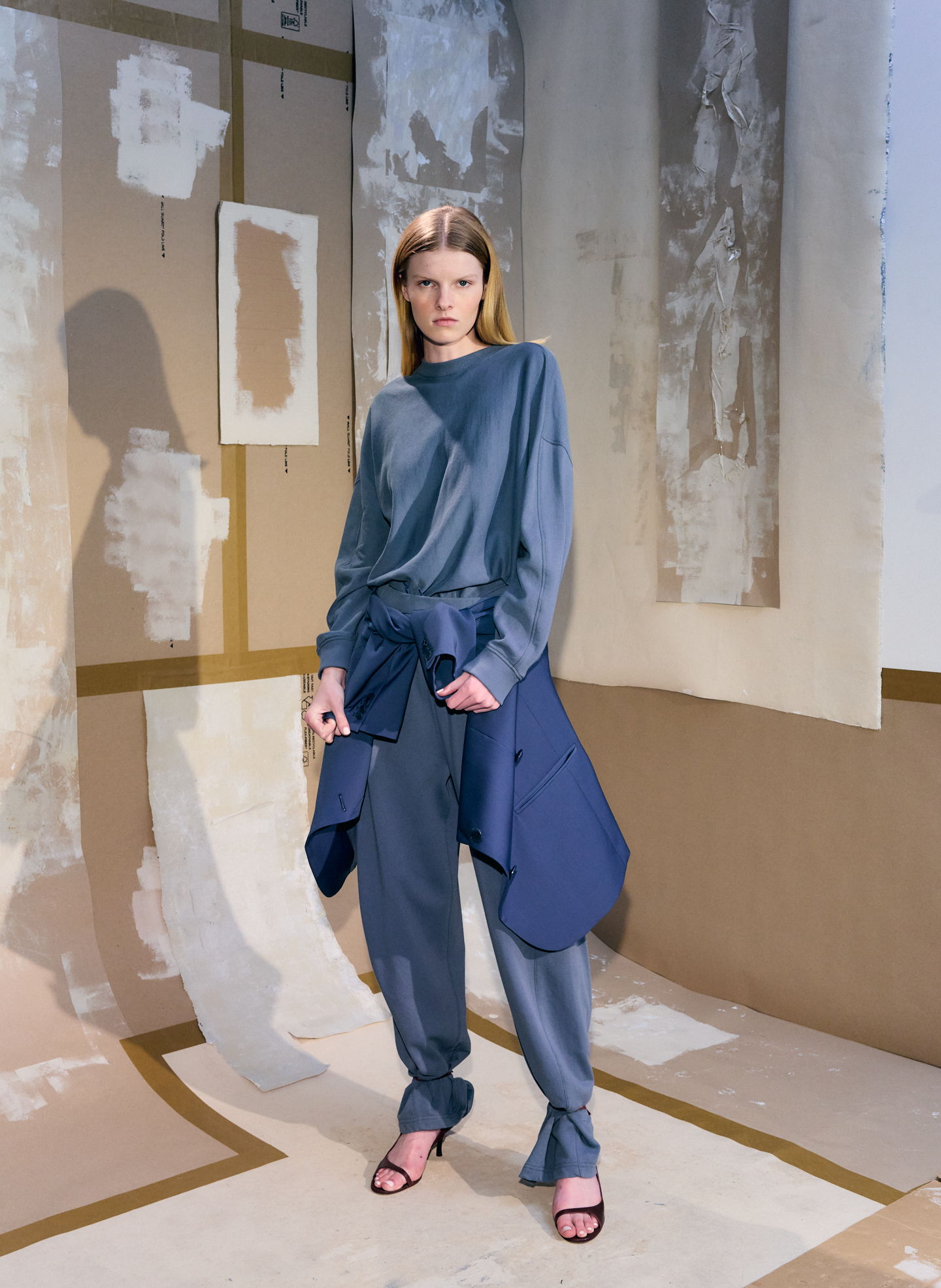 Model in stylish blue outfit posing against artistic backdrop.