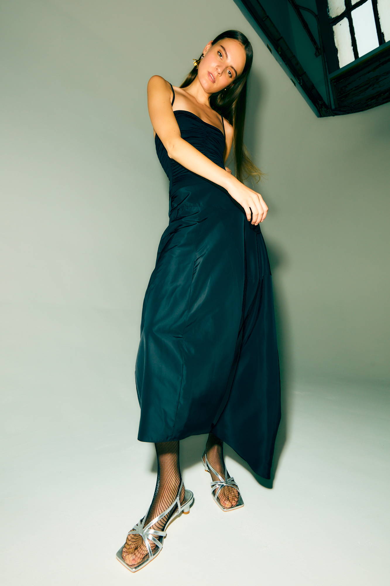 Model wearing a dark dress and silver sandals against a neutral background.