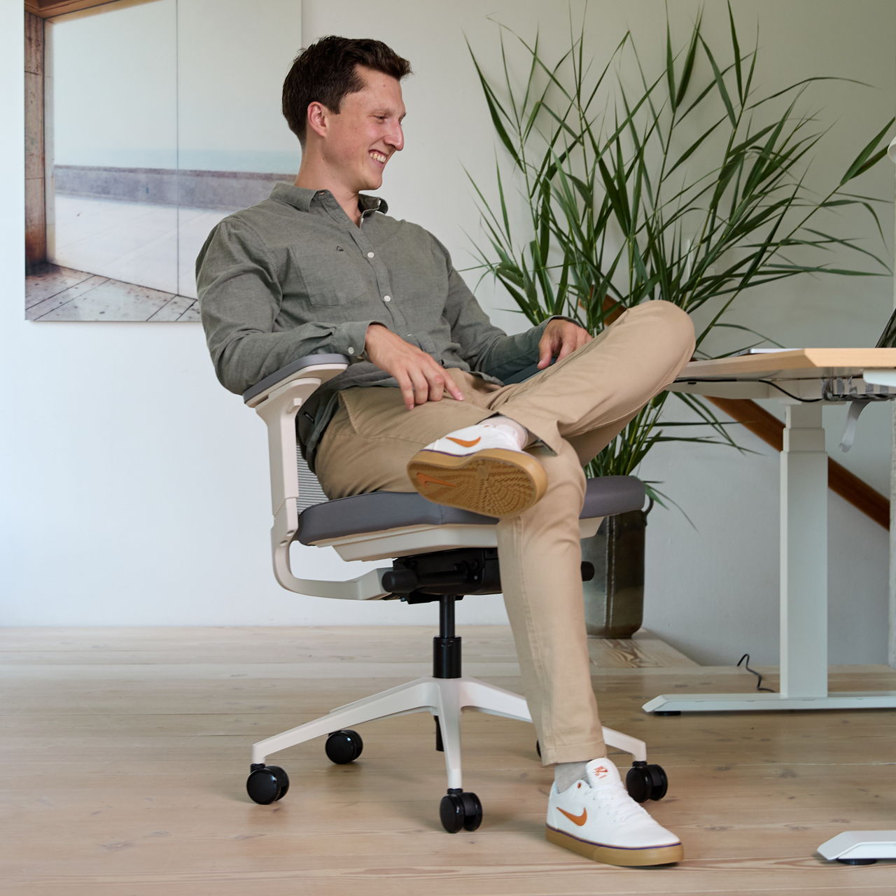 Un jeune homme est assis sur un siège de bureau ofinto Active blanc Active semble très satisfait de son siège ergonomique et confortable