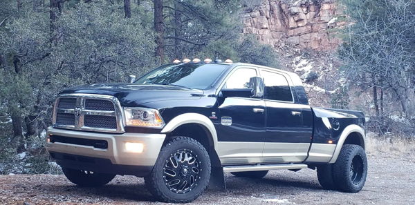 Front three-quarter view of two-tone black and tan Ram 3500 dually parked on gravel in wooded mountain setting