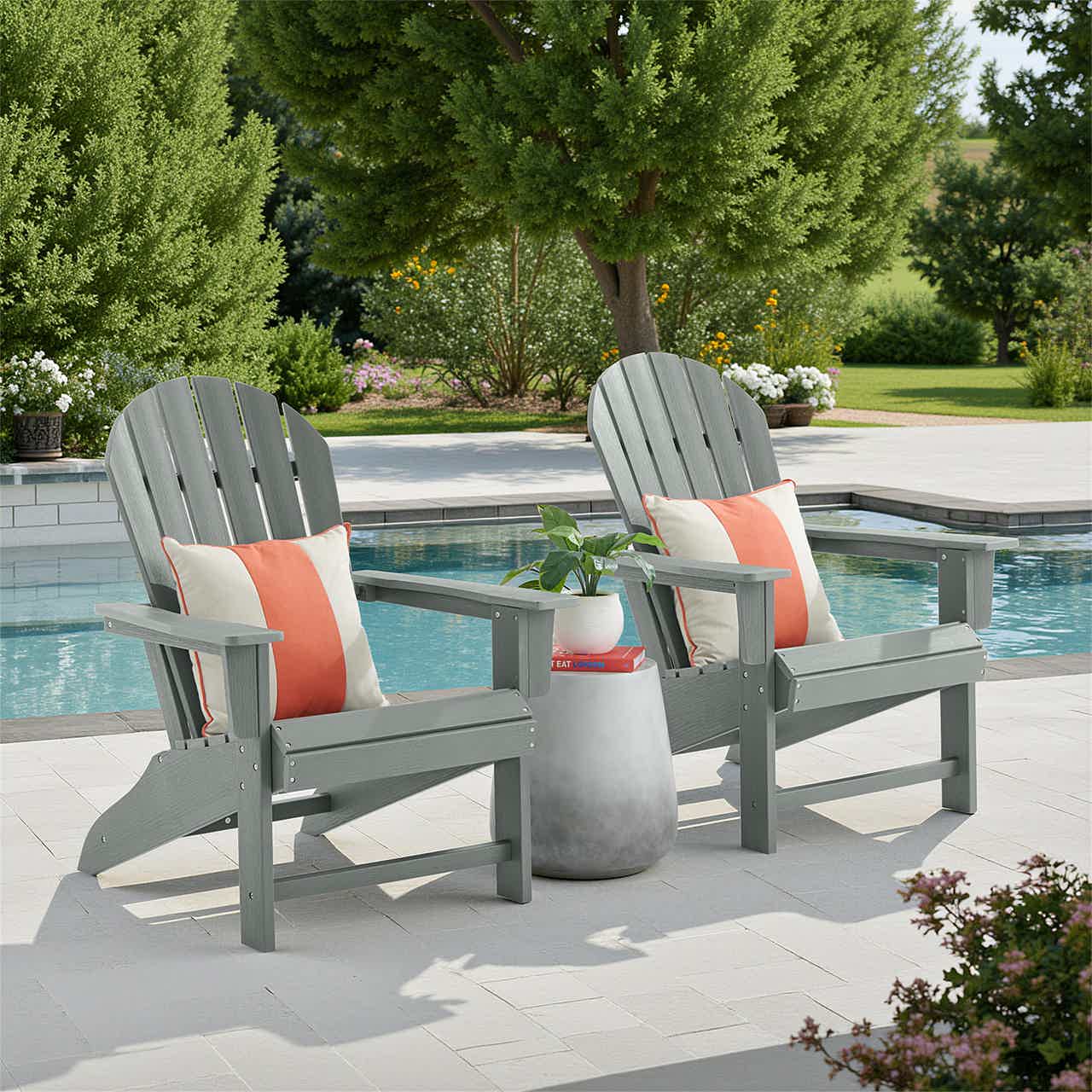Two gray Adirondack chairs with cushions by a pool surrounded by greenery.