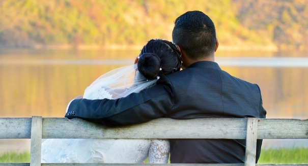 engaged couple sitting on a park bench overlooking a lake with beautiful trees turning different fall colors in the distance