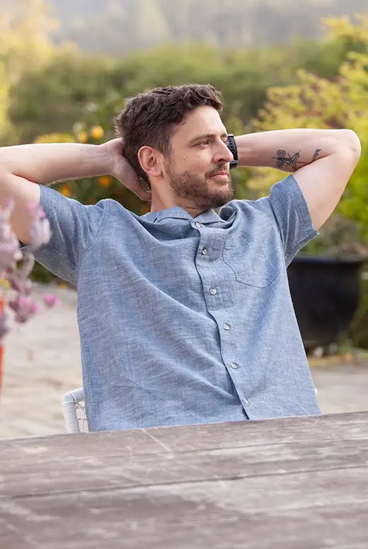 Man relaxing outdoors at a table, with hands behind his head.