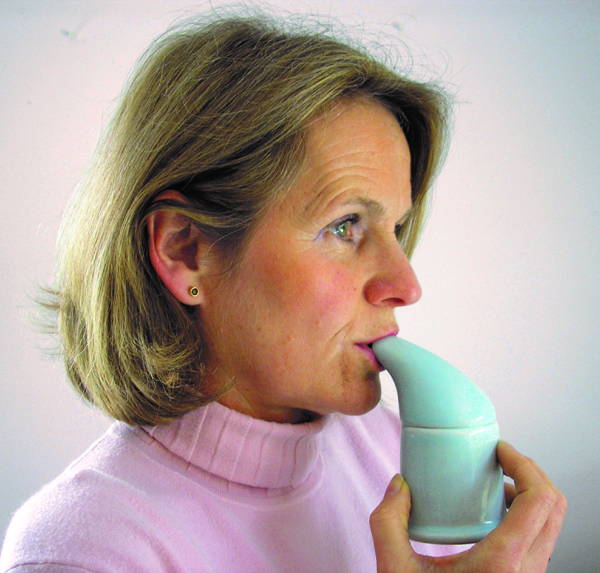 older woman wearing pink turtleneck, holding salt inhahler at lips