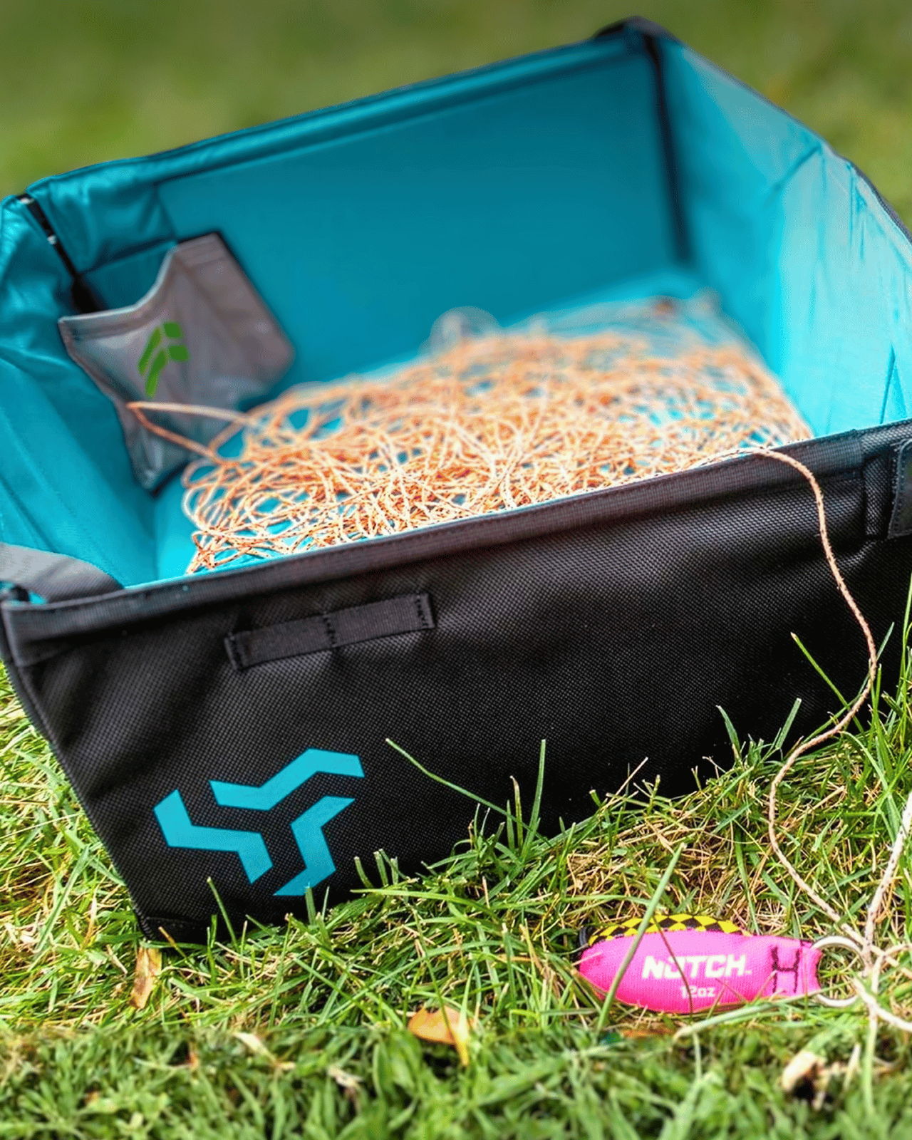 A black and turquoise container filled with tangled cords on grass.