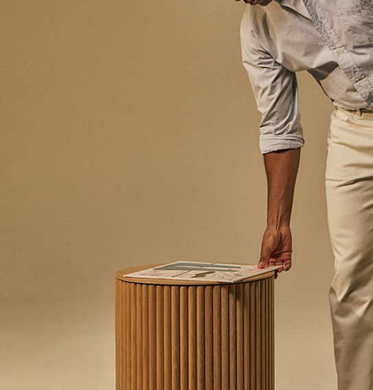 A person placing items on a wooden round table against a neutral background.