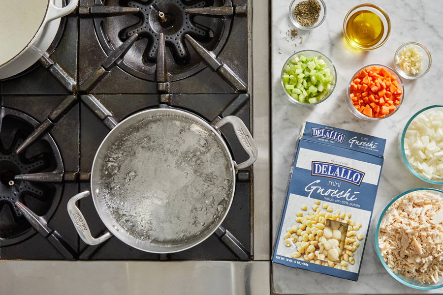 Pot of boiling water on stove with ingredients on the counter beside it.