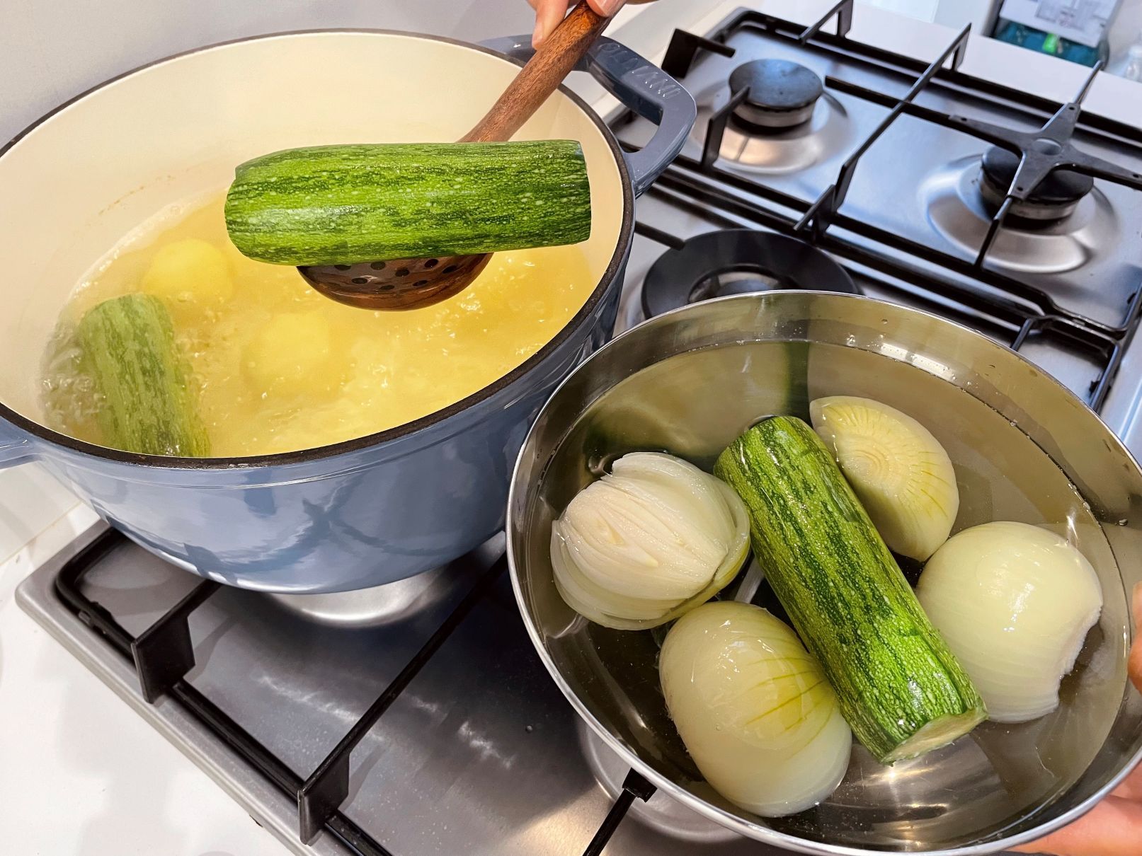 Cucumbers and onions being cooked in pots on a stove.