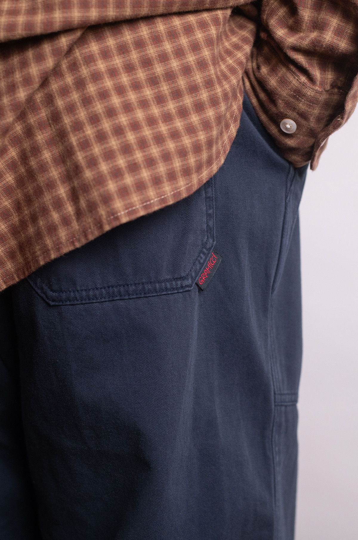 Person wearing a brown checkered shirt, navy pants, and white shoes.