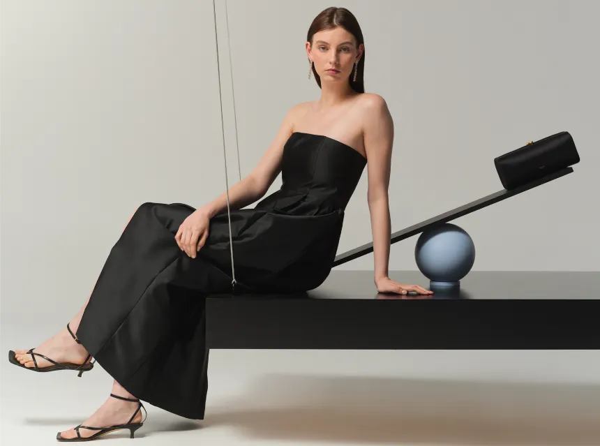 Woman in a black strapless dress sitting on a black platform with geometric objects.