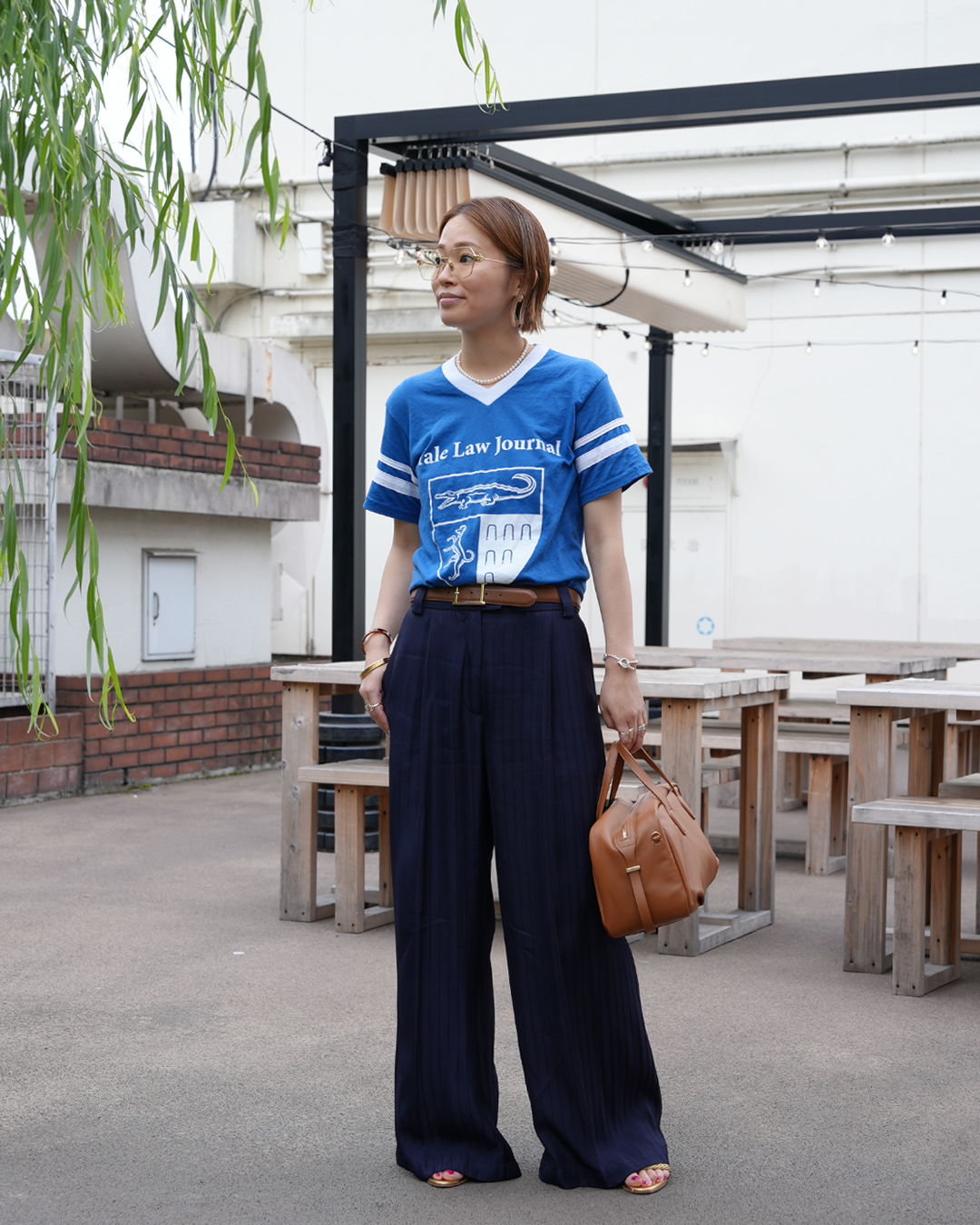 Person standing outdoors in casual outfit with blue shirt and wide pants.