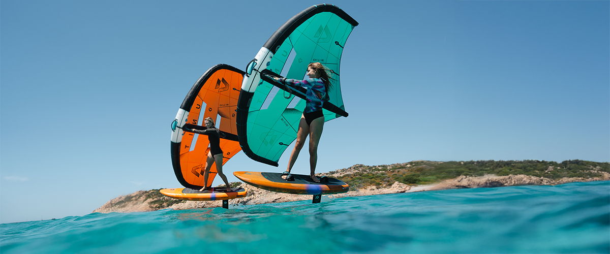 Two people surfing on foil boards with colorful sails in the ocean.