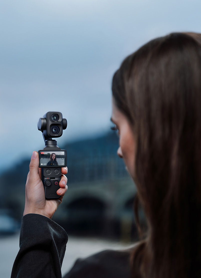 A person holding a DJI Osmo Pocket 4P camera outdoors, facing a scenic background.