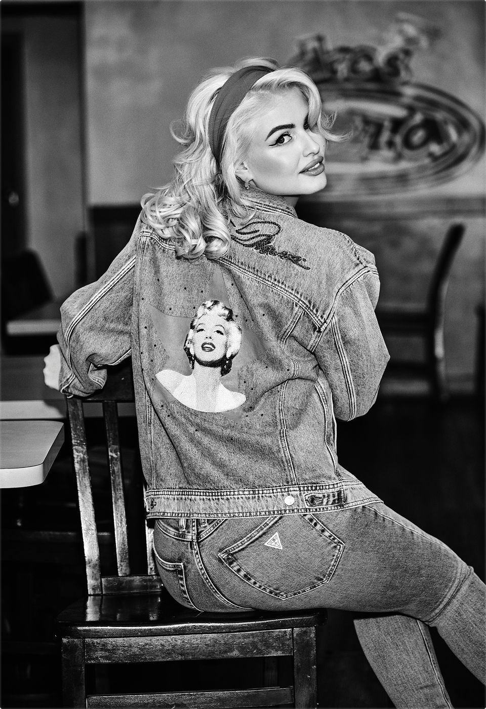 Woman in denim jacket with a Marilyn Monroe graphic, sitting on a chair.