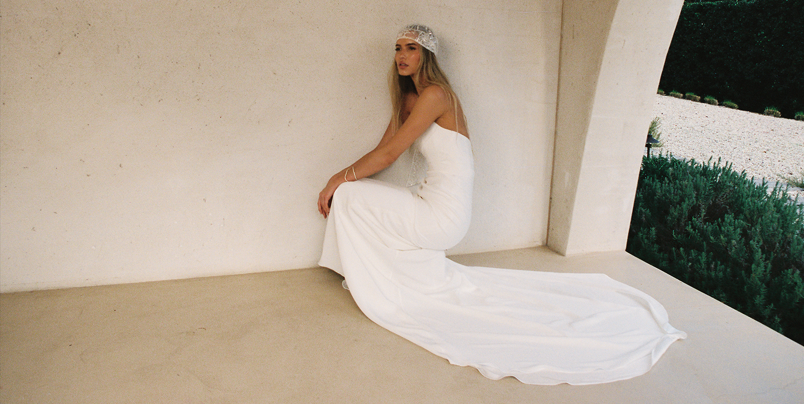 Woman in a white dress sitting against a wall, with a flowing train.