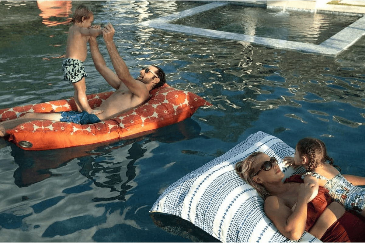 Family relaxing on patterned pool floats in a backyard swimming pool, adding a playful element to summer entertaining.