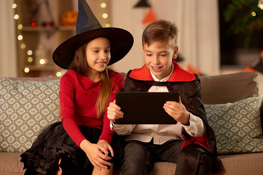 boy and girl sitting on couch in costumes and smiling at a tablet