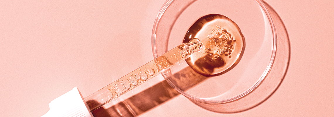 A dropper with liquid on a pink background.