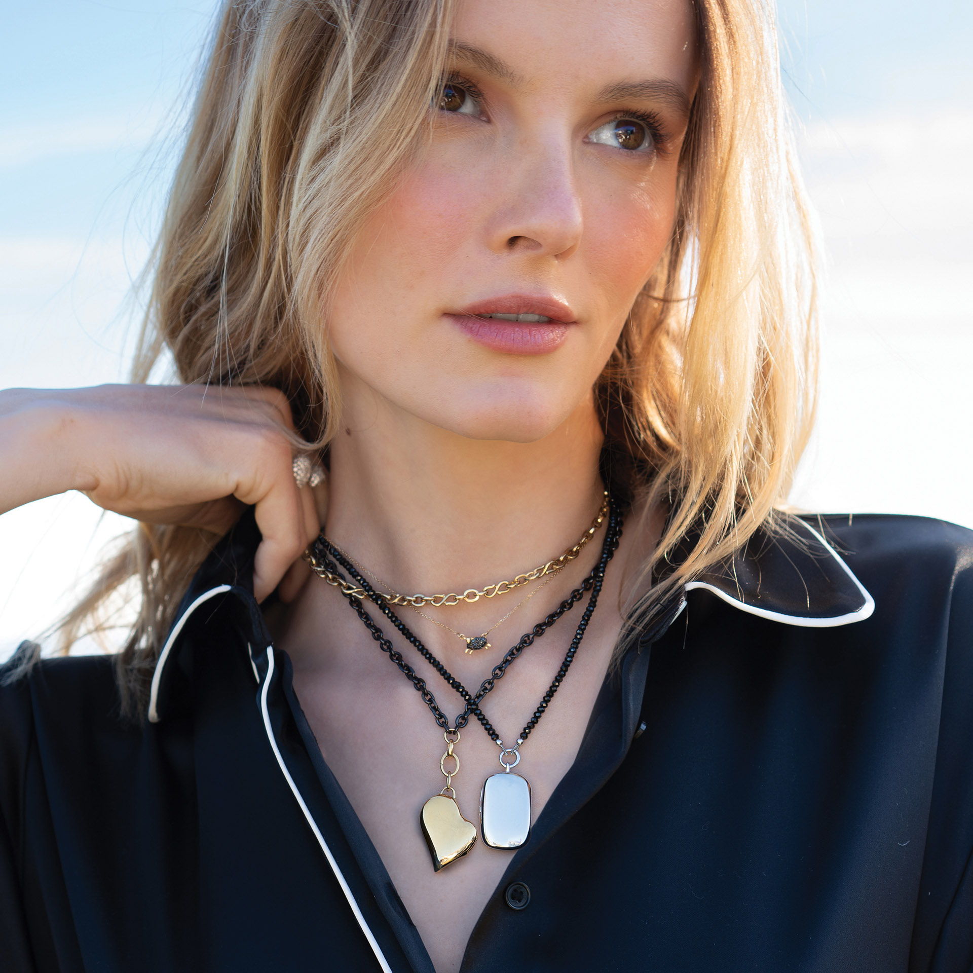 Woman wearing layered necklaces, with a scenic background and a thoughtful expression.
