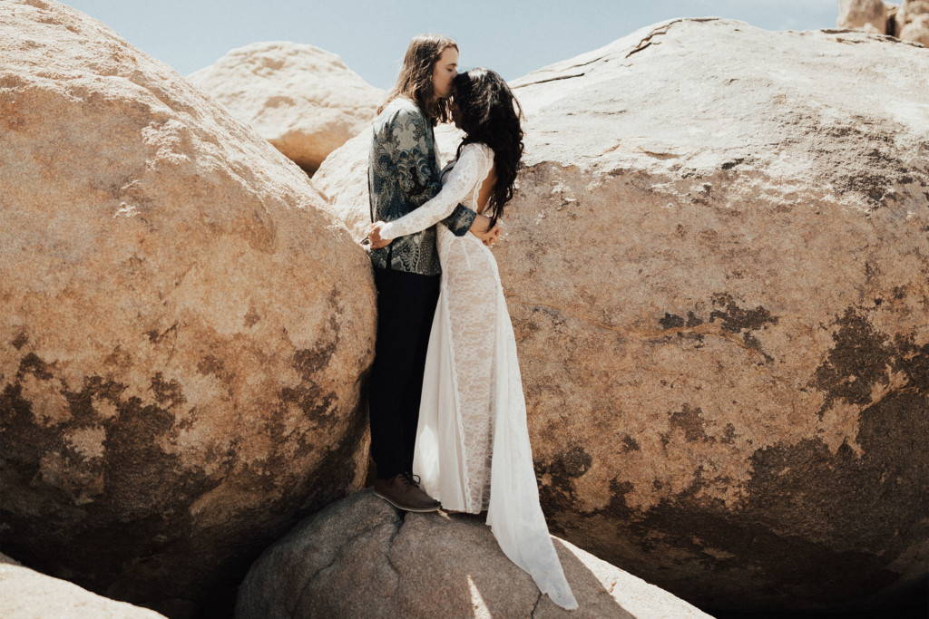 Bride in long sleeve lace dress hugging groom in desert scape