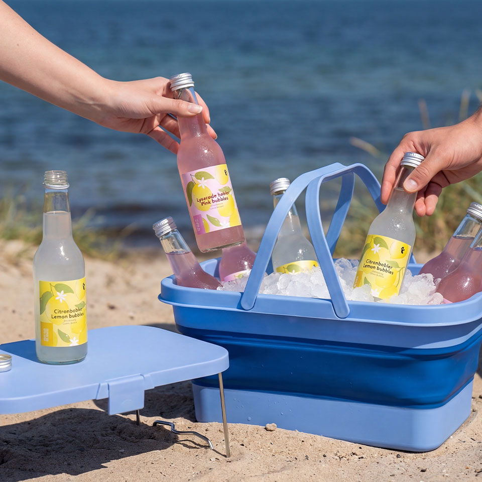 Hands reaching for bottles from a blue cooler on the beach.