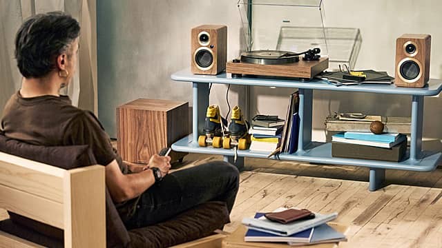 Person sitting on a couch, listening to a record player with speakers.