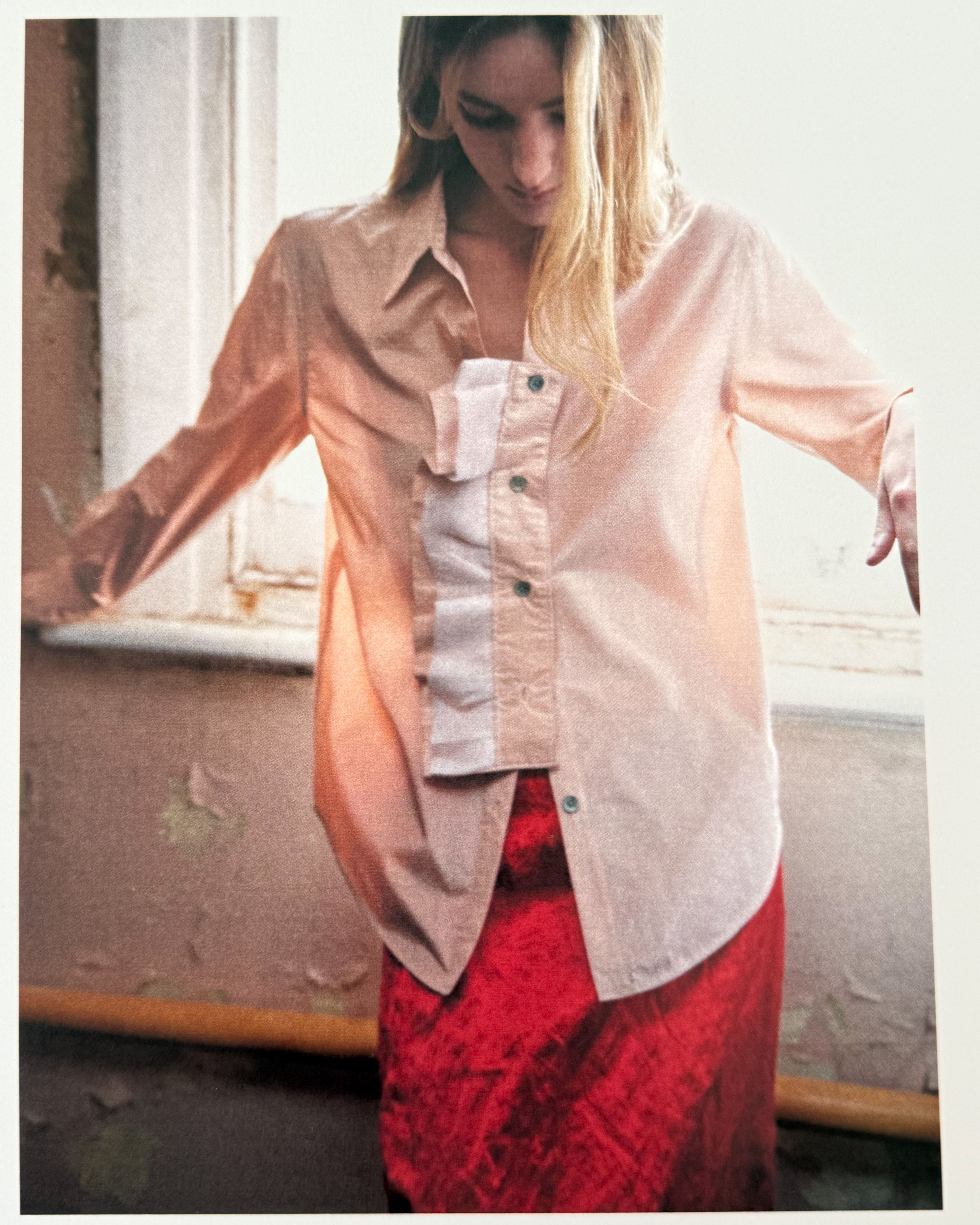 A woman in a layered outfit poses near a window.