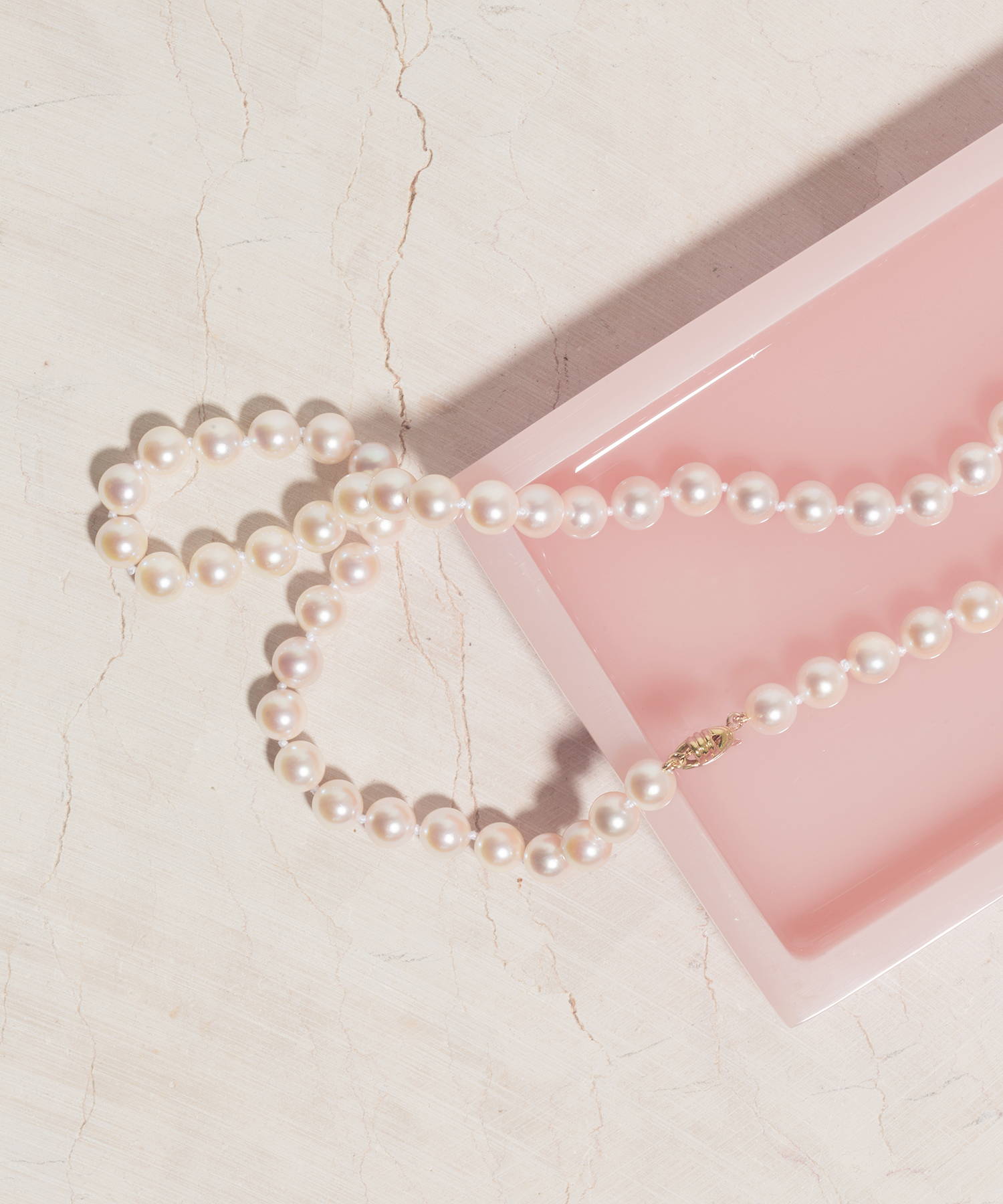 White cultured pearl necklace on a pink tray with a marble countertop