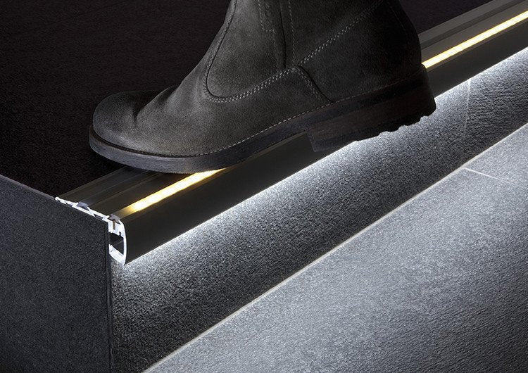 LED profile run under the stair nosing, lighting the tread below as a foot steps onto it