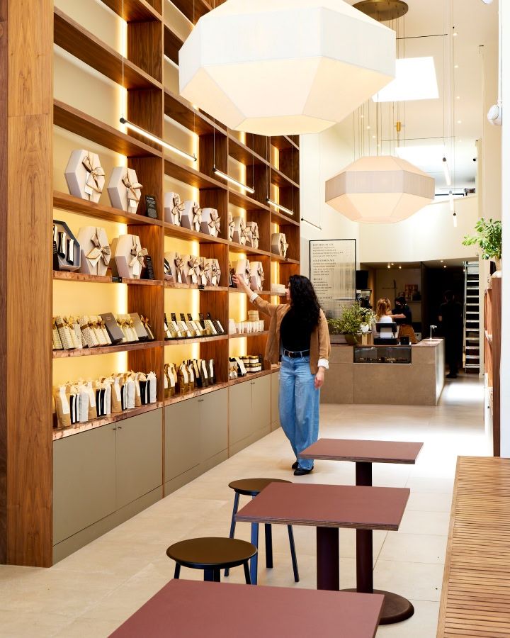 A woman walking in a modern café with wooden shelves and tables.