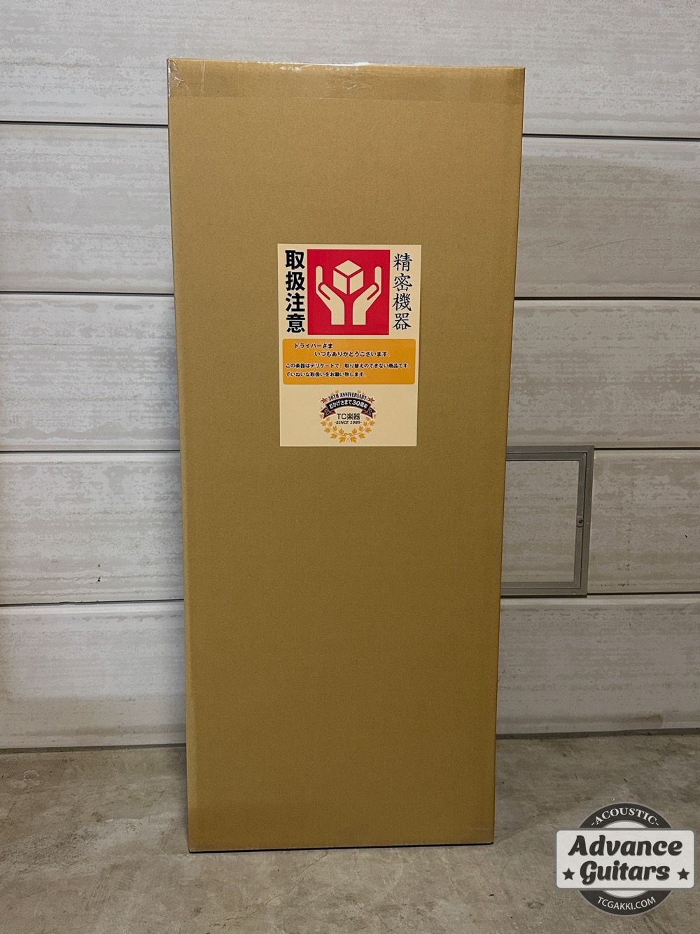 Cardboard box with labels, standing upright against a wall.