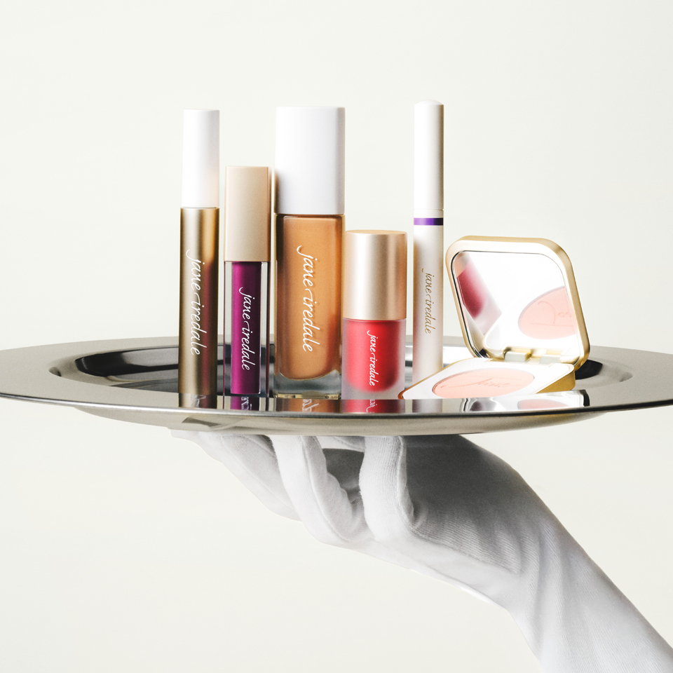 A hand holding a tray with various cosmetic products.