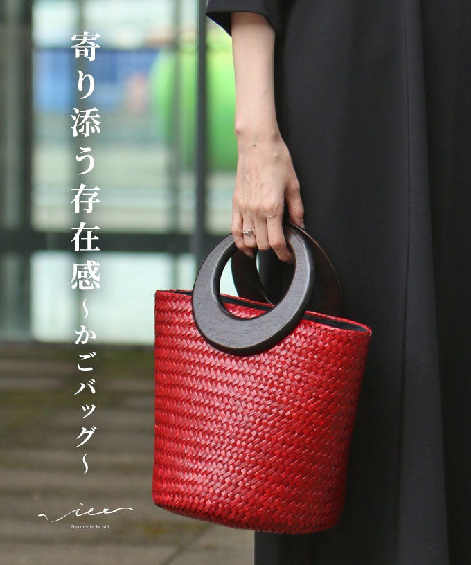 A person holding a red woven handbag with a round handle.