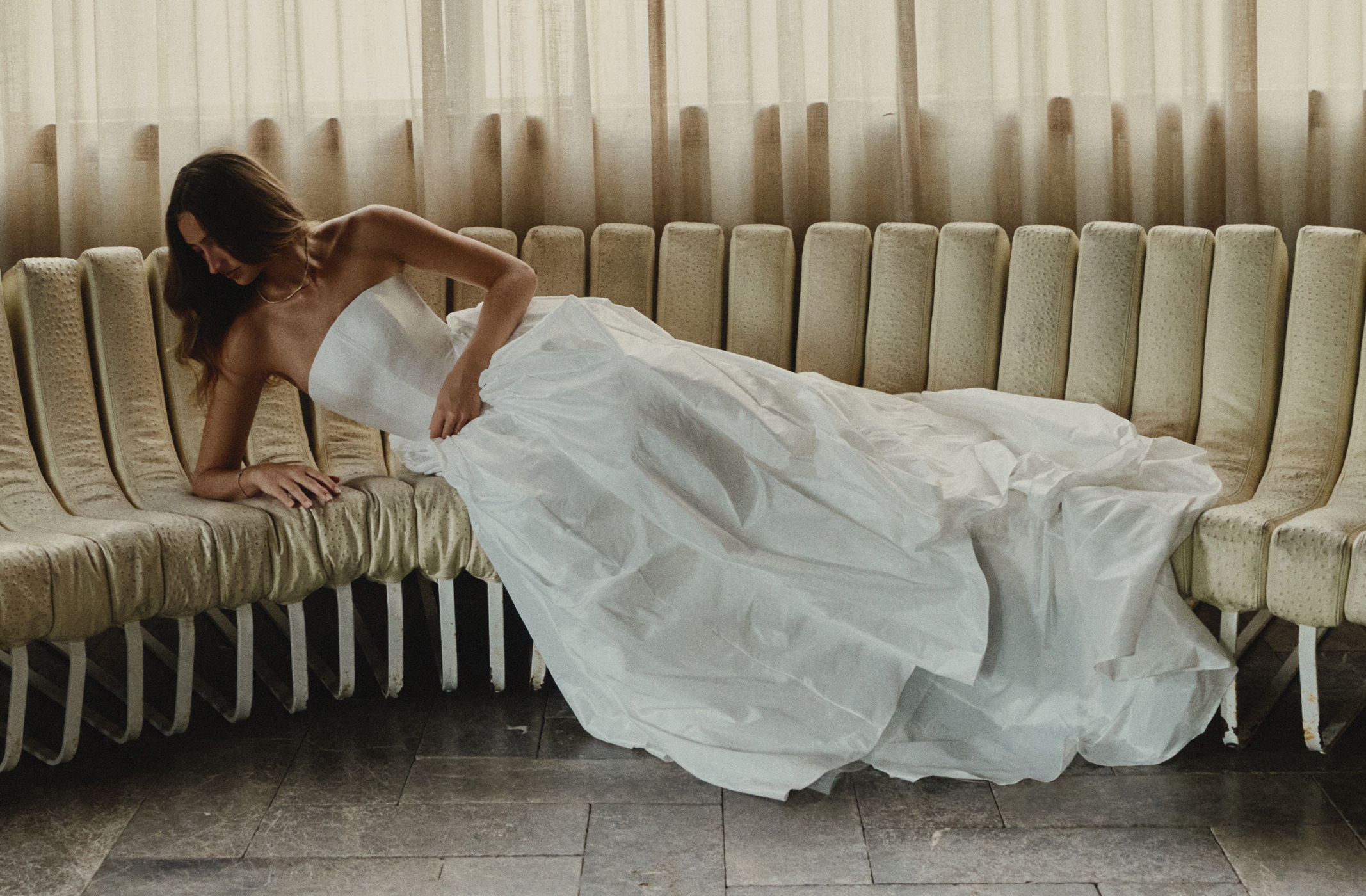 Bride in a white dress reclining on a curved sofa.