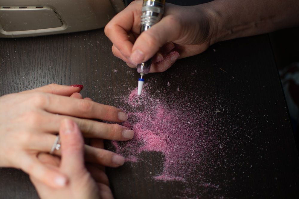 A person applying pink nail powder to another person's hands.