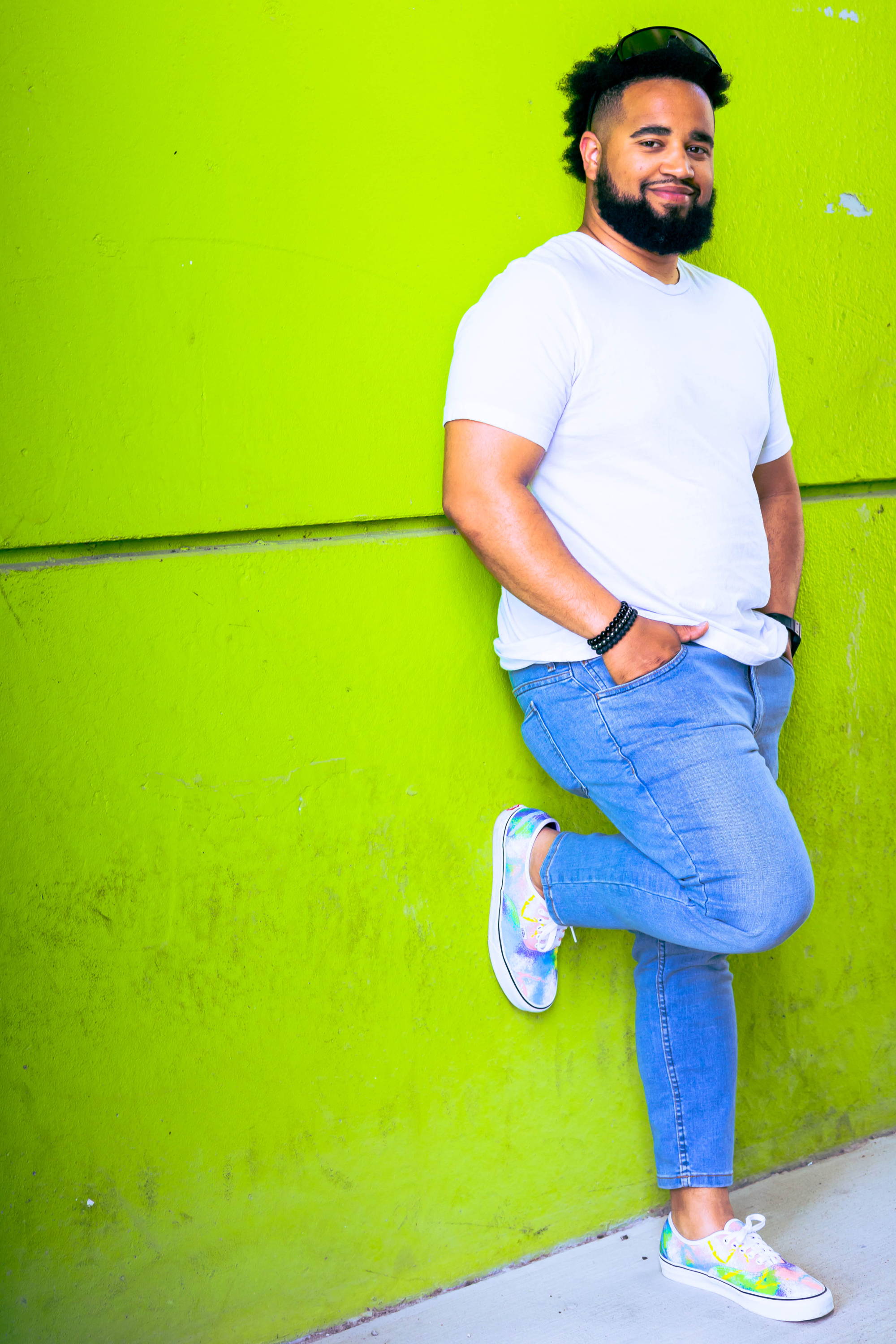 Happy guy leaning on green wall wearing white t shirt and light blue wash xavier jeans from under510.com
