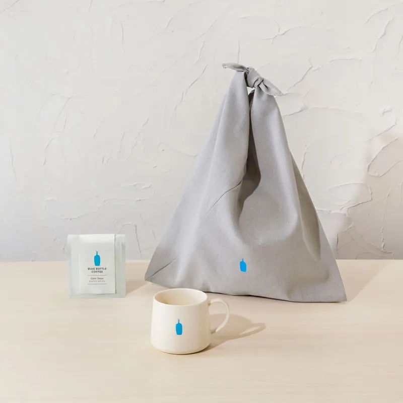 Gray fabric bag, white cup, and box on a wooden surface.
