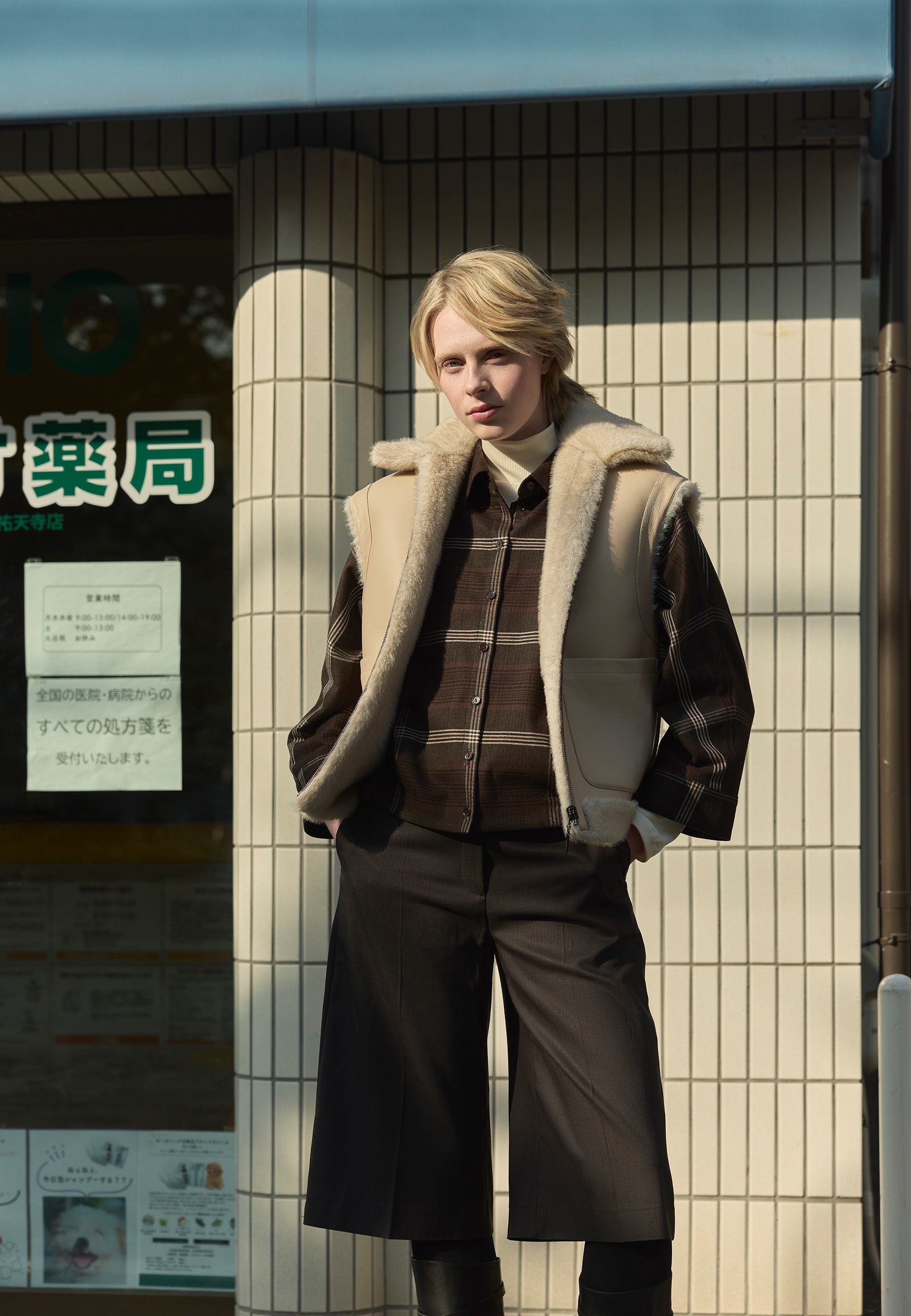 A person in a stylish outfit poses against a tiled wall.