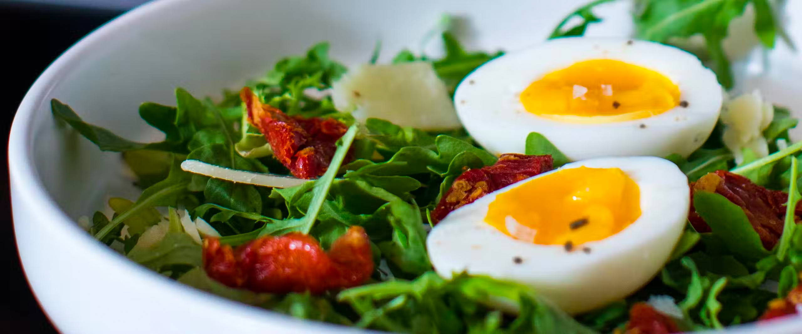 bowl with arugula salad with two halves of jammy eggs on top.