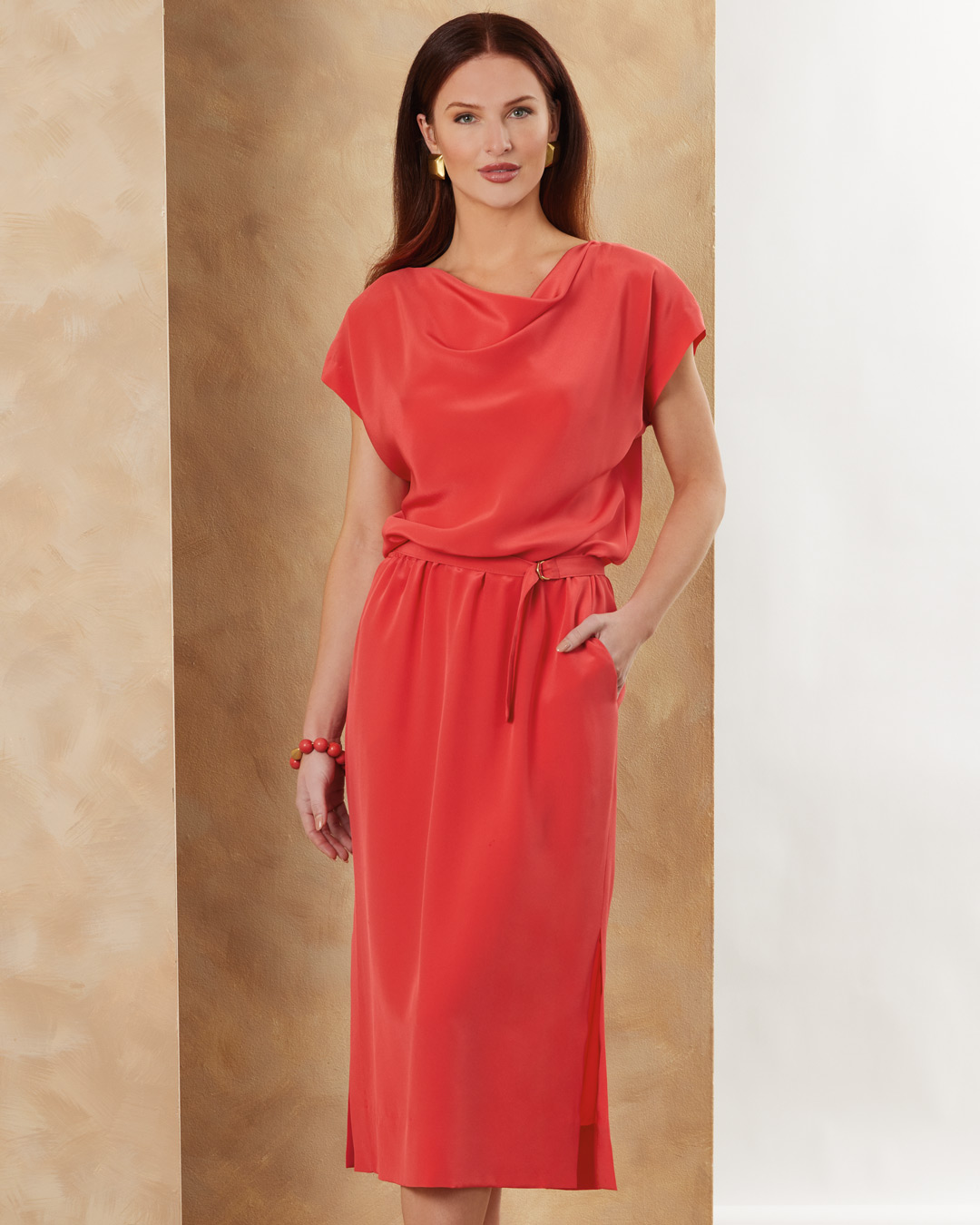 Woman in a coral dress with a belt, standing against a neutral background.