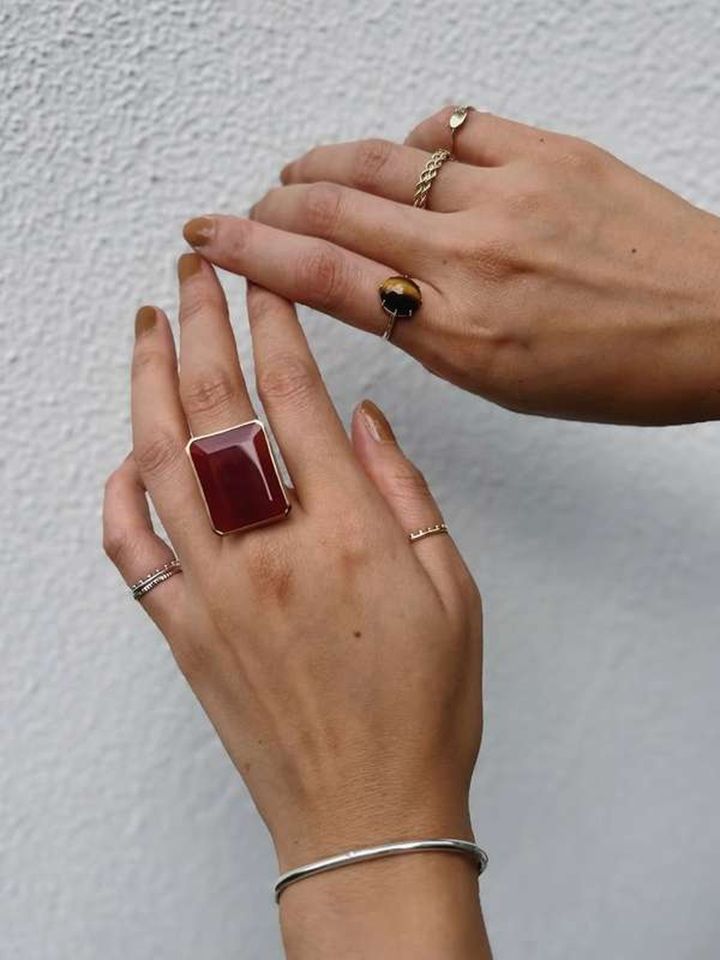 Hands with rings and a large red stone ring against a white background.